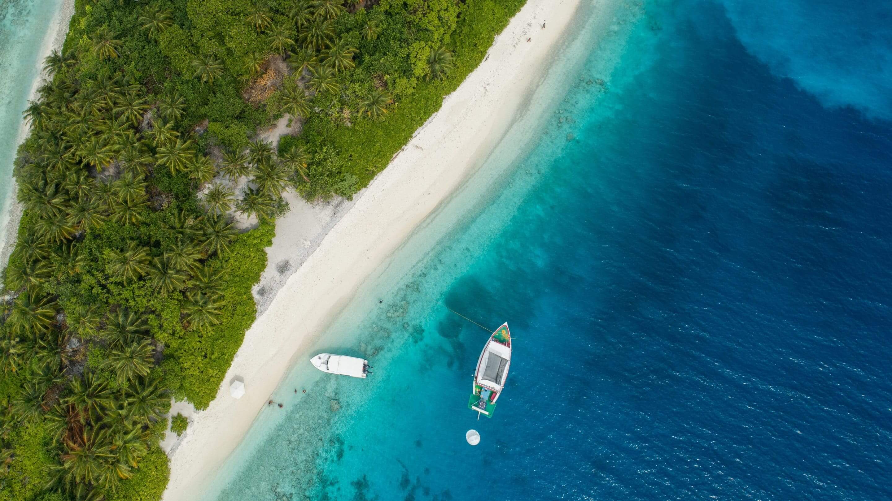 crystal clear beach with a couple of boats anchored off the coast. aerial view - do you need a passport to go to the Bahamas?