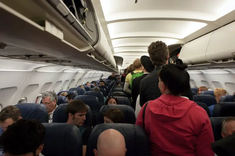 Inside of a plane with people entering and loading their things in the overhead bin - Can you bring pepper spray on a plane?